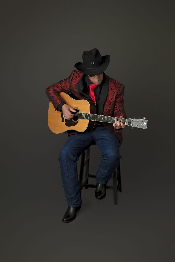 Cowboy hat musician seated playing acoustic guitar